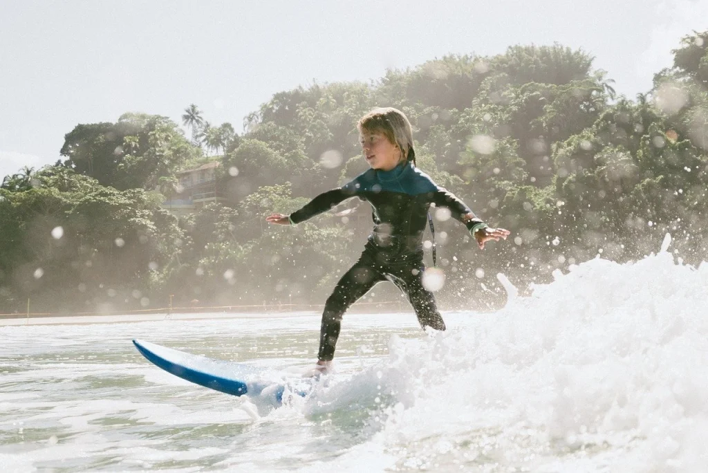 Kind steht selbstbewusst auf Surfbrett auf einer Welle