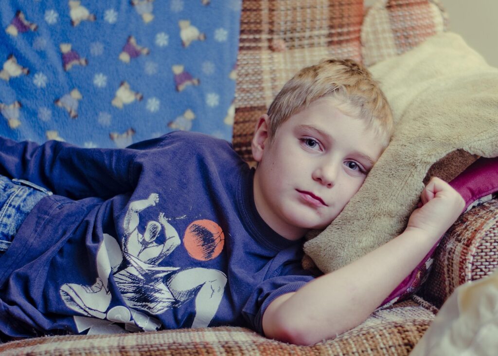Junge liegt auf einem Sofa mit blauen T-Shirt und ist krank hat Bauchschmerzen und ist traurig