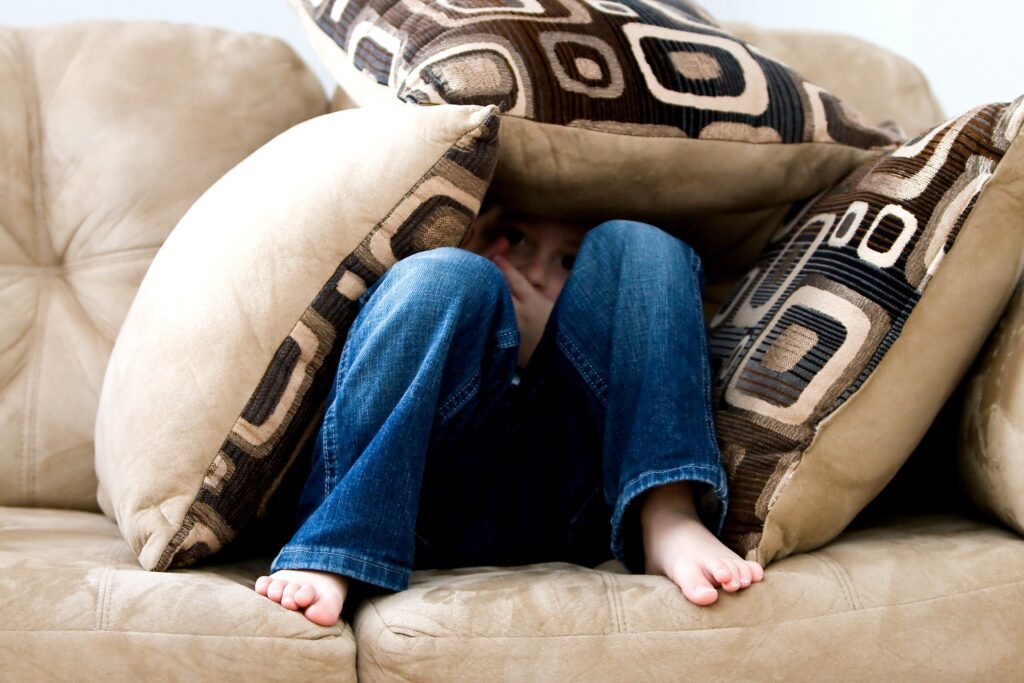 Kind in blauer Hose Jeans versteckt sich in Kissen einer Burg auf dem Sofa hat Angst macht sich eine Höhle