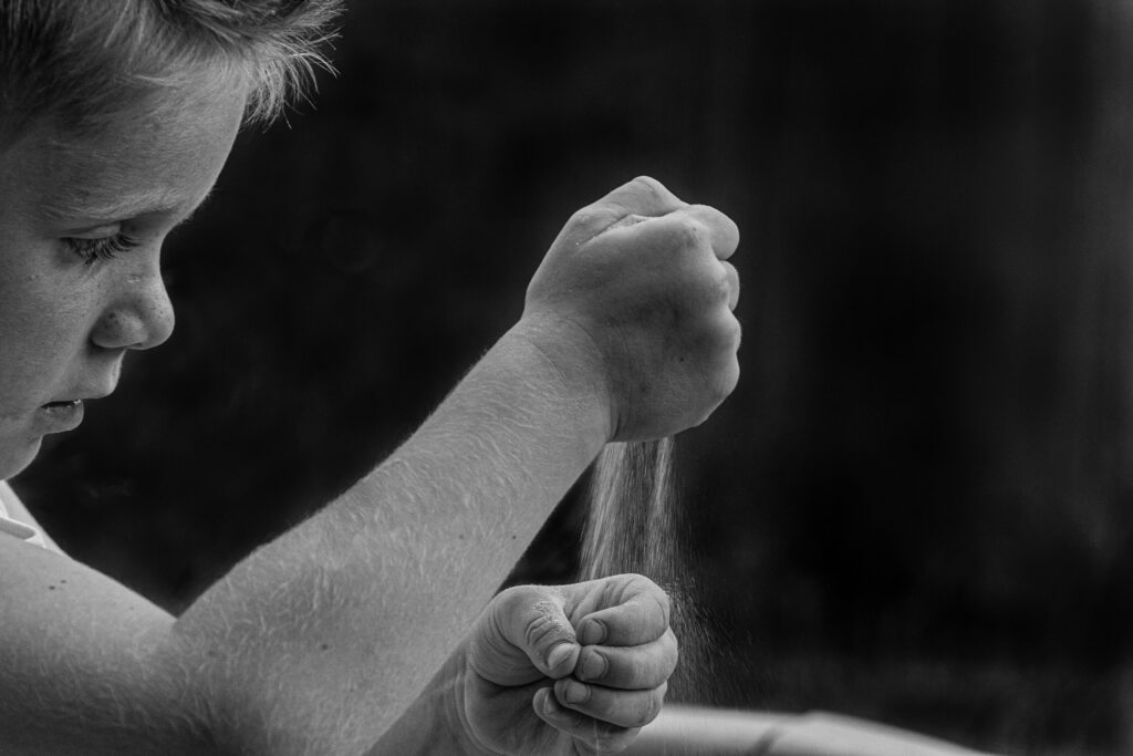 Junge spielt mit Sand in der Hand zur Selbstregulation von Emotionen und Gefühlen schwarz weiss