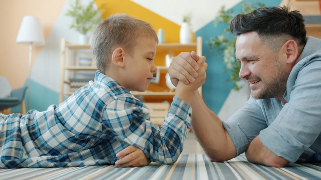 junge mit Vater am Armdrücken selbstbewusst stark Freude Vertrauen auf Teppich im Zimmer